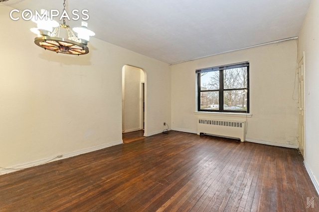 spare room with dark wood-style flooring, arched walkways, baseboards, a chandelier, and radiator heating unit
