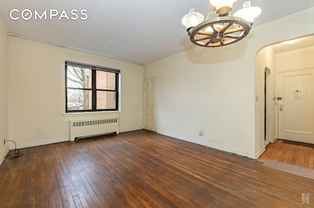 empty room with arched walkways, baseboards, wood-type flooring, a chandelier, and radiator