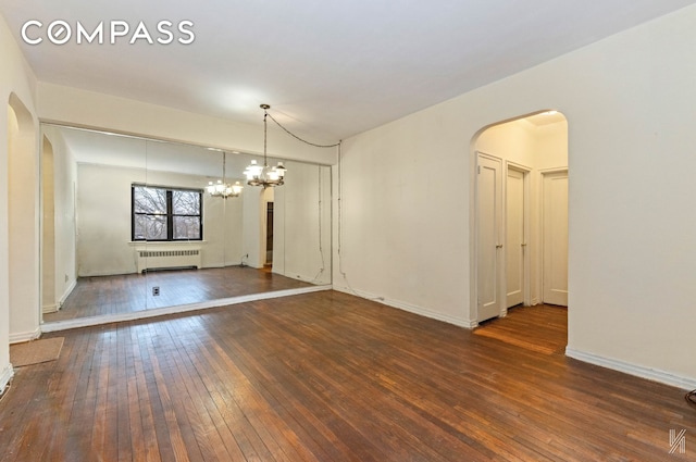 empty room featuring an inviting chandelier, radiator, wood-type flooring, and arched walkways