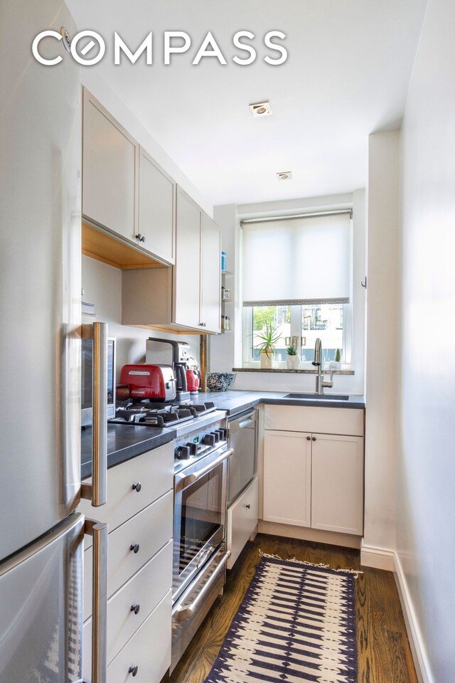 kitchen with a sink, stainless steel appliances, dark countertops, white cabinets, and dark wood-type flooring