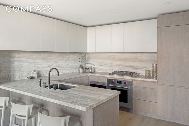 66 Clinton St Unit 5B, New York City, NY 10002 - kitchen featuring stainless steel appliances, a peninsula, a breakfast bar, light countertops, and backsplash
