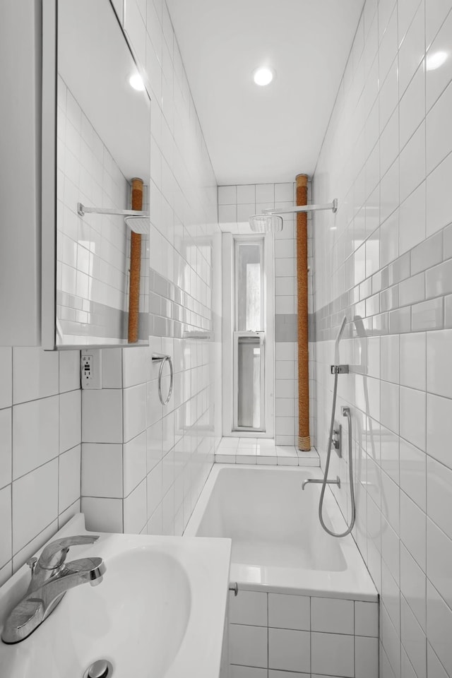 full bath featuring a relaxing tiled tub, tile walls, and a sink