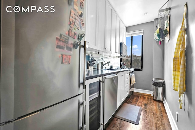 kitchen with appliances with stainless steel finishes, baseboards, dark countertops, white cabinets, and dark wood-style flooring