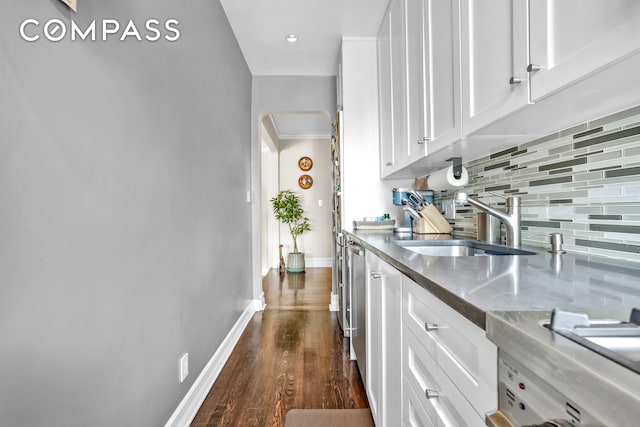 interior space with dark wood-style flooring, baseboards, tasteful backsplash, white cabinetry, and a sink