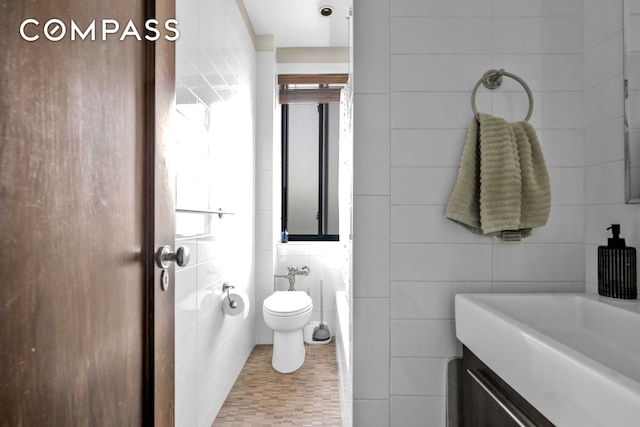 bathroom with toilet, vanity, and tile walls