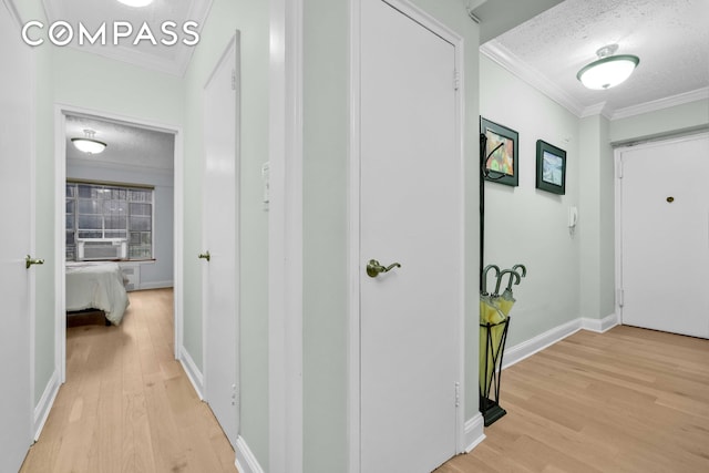 hallway featuring light wood-type flooring, ornamental molding, and a textured ceiling