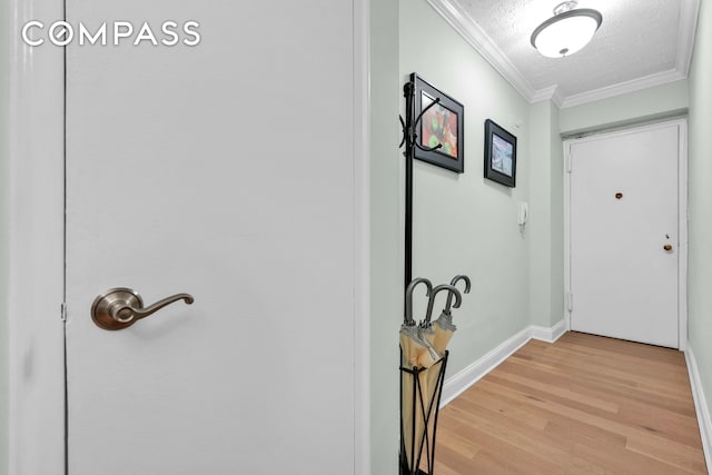 interior space featuring a textured ceiling, ornamental molding, baseboards, and light wood-style floors