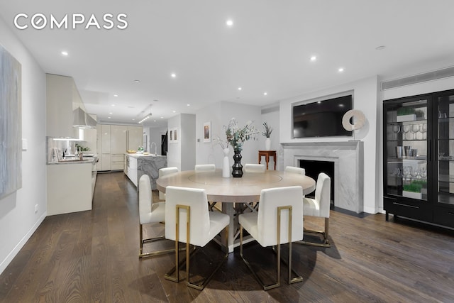 dining space featuring recessed lighting, a high end fireplace, baseboards, and dark wood-style floors
