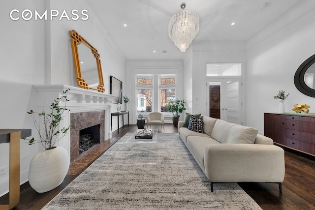living area with a high end fireplace, dark wood-style floors, an inviting chandelier, ornamental molding, and recessed lighting