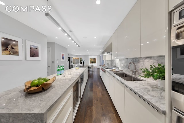 kitchen with white cabinets, dark wood-style flooring, light stone counters, a sink, and modern cabinets