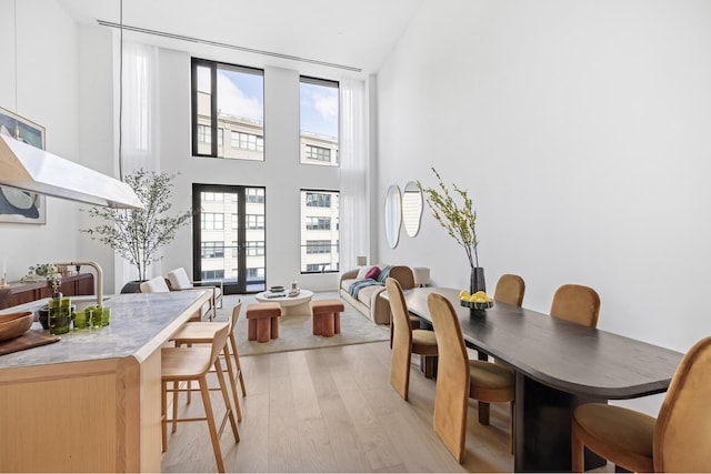 dining area with light wood-style flooring, a healthy amount of sunlight, and a high ceiling