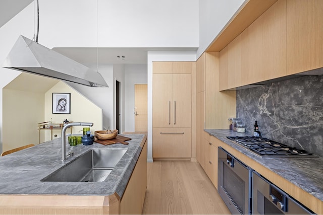 kitchen with light wood-style floors, stainless steel gas stovetop, a sink, light brown cabinets, and backsplash