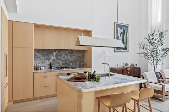 kitchen with light brown cabinets, light countertops, a kitchen bar, gas stovetop, and decorative backsplash