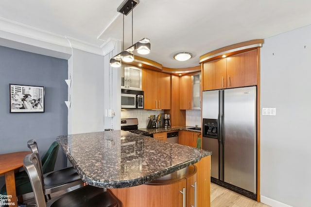 kitchen featuring glass insert cabinets, a kitchen breakfast bar, brown cabinetry, tasteful backsplash, and appliances with stainless steel finishes