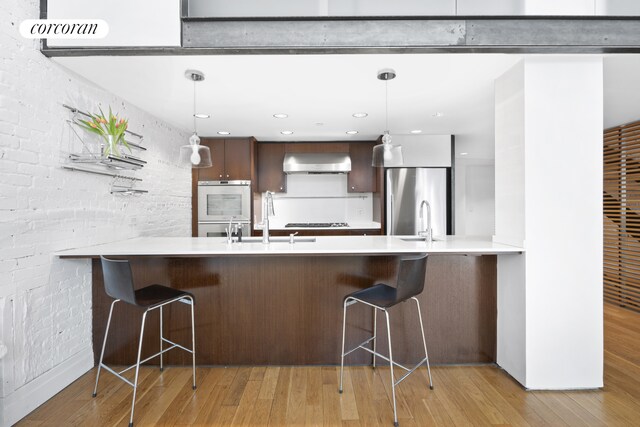 53 Crosby St Unit 1, New York City, NY 10012 - kitchen featuring stainless steel appliances, a peninsula, wall chimney range hood, and light countertops