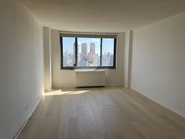 2025 Broadway Unit 23G, New York City, NY 10023 - empty room with wood finished floors, a skyline view, and radiator