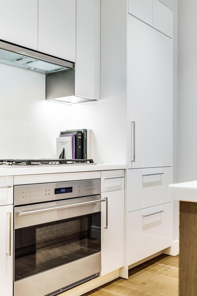 230 E 20th St Unit 11, New York City, NY 10003 - kitchen featuring oven, under cabinet range hood, light wood-type flooring, white cabinetry, and light countertops