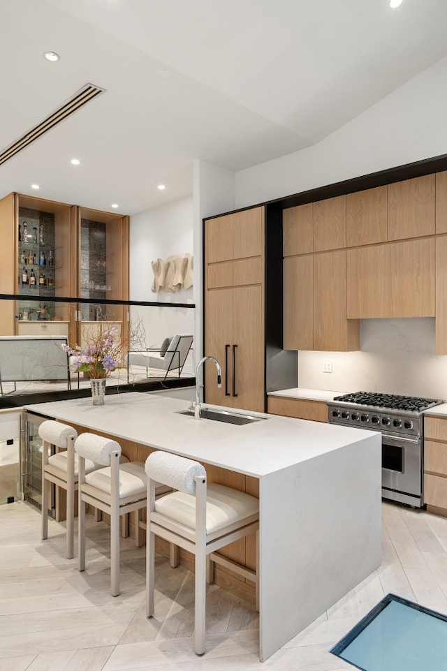 kitchen with light brown cabinets, modern cabinets, high end stove, and a sink