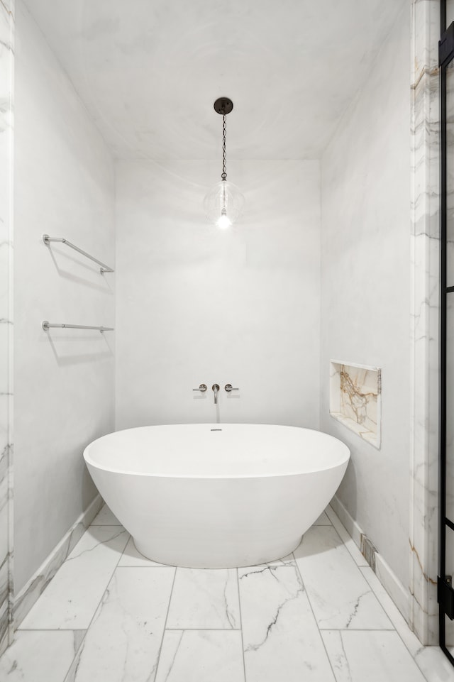 bathroom with a freestanding tub, marble finish floor, and baseboards