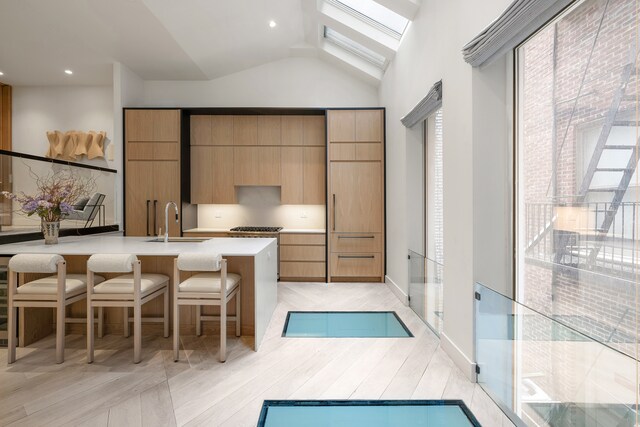 kitchen with vaulted ceiling with skylight, a sink, a breakfast bar, light countertops, and modern cabinets