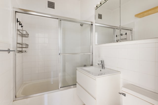 full bathroom featuring tile walls, toilet, vanity, and shower / bath combination with glass door