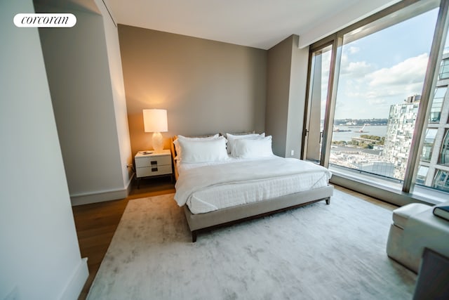 bedroom with multiple windows, a water view, wood finished floors, and baseboards