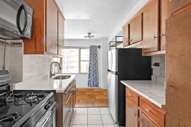 kitchen with a sink, appliances with stainless steel finishes, brown cabinetry, and decorative backsplash