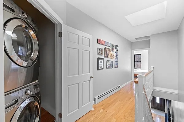 laundry area featuring light wood-type flooring, a baseboard radiator, laundry area, and stacked washer and dryer