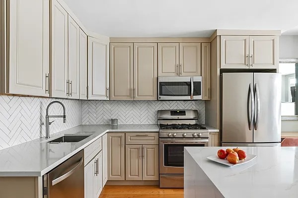 kitchen with backsplash, appliances with stainless steel finishes, light wood-type flooring, a sink, and light countertops