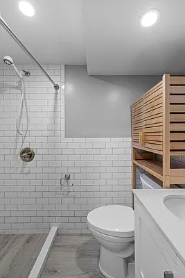 bathroom featuring vanity, toilet, tile walls, recessed lighting, and a tile shower
