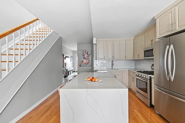 kitchen with decorative backsplash, a kitchen island, light wood-type flooring, cream cabinets, and appliances with stainless steel finishes