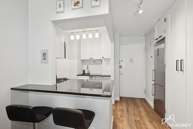301 E 22nd St Unit 12H, New York City, NY 10010 - kitchen featuring track lighting, stainless steel fridge, white cabinetry, and a peninsula