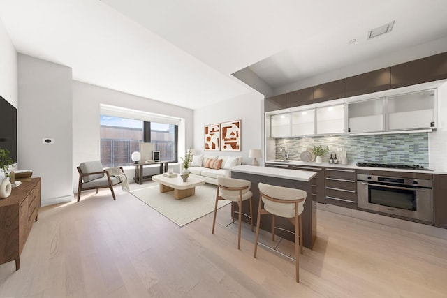 75 Wall St Unit 28-Q, New York City, NY 10005 - kitchen featuring oven, gas cooktop, light wood-style floors, a breakfast bar, and tasteful backsplash