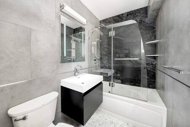 bathroom featuring tile walls, bath / shower combo with glass door, vanity, and toilet