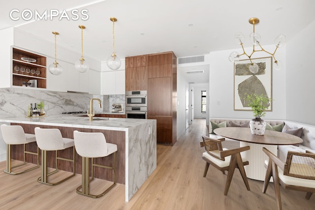 kitchen with modern cabinets, a peninsula, tasteful backsplash, double oven, and a breakfast bar