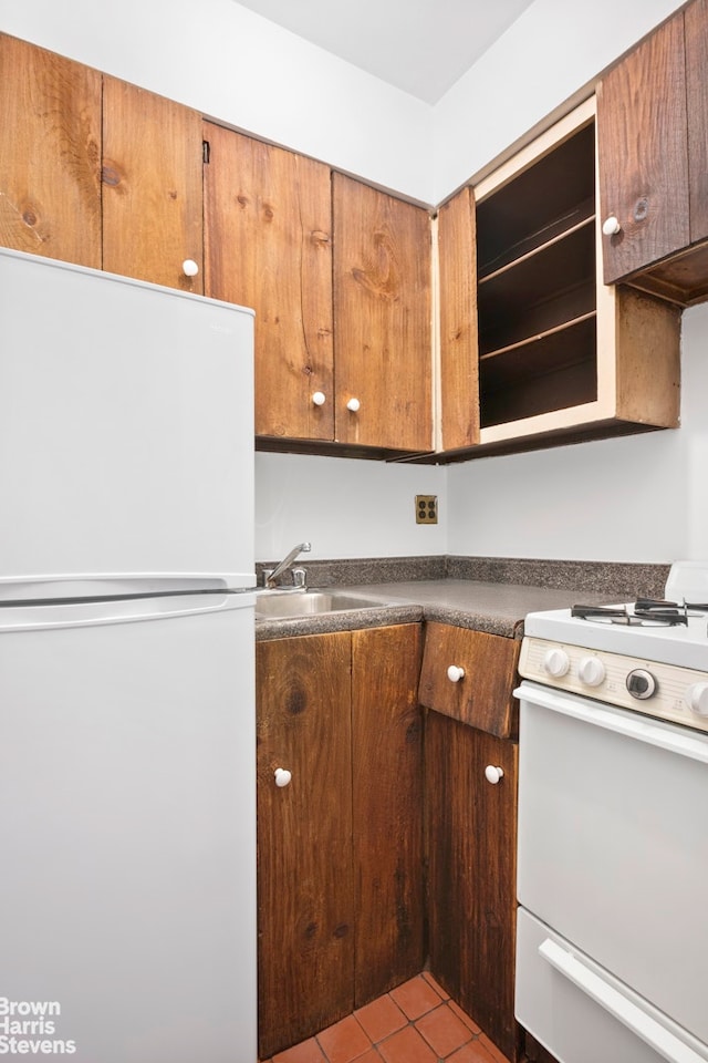 kitchen featuring white appliances, a sink, tile patterned floors, and dark countertops