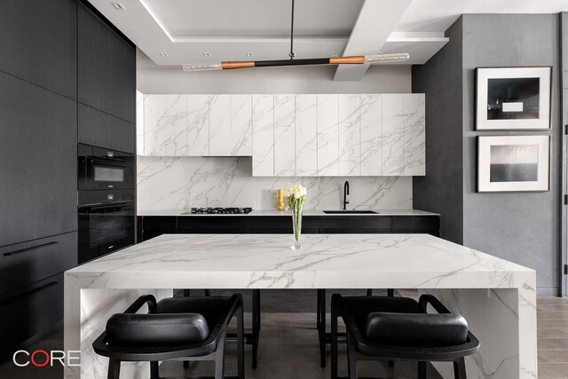 30 E 10th St Unit 10N, New York City, NY 10003 - kitchen featuring light stone countertops, a sink, dark cabinetry, black oven, and a breakfast bar area