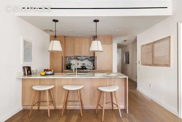 kitchen with a peninsula, decorative backsplash, light wood-style floors, baseboards, and a breakfast bar