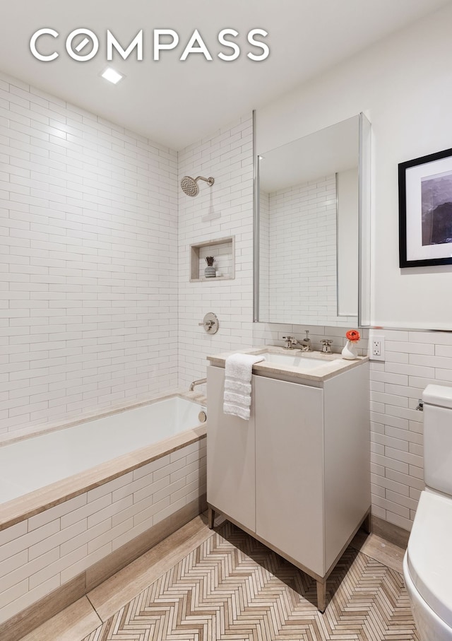 full bath with tile walls, toilet, tiled shower / bath, vanity, and tile patterned flooring
