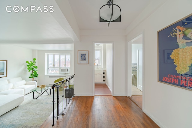 hall with wood finished floors, radiator, an upstairs landing, baseboards, and a sink