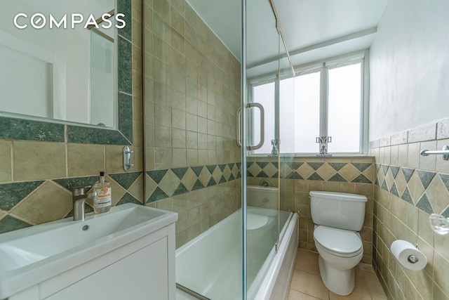 full bath with tile walls, toilet, combined bath / shower with glass door, vanity, and tile patterned flooring