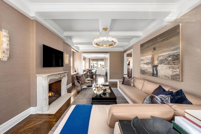 living room featuring a premium fireplace, a chandelier, coffered ceiling, baseboards, and ornamental molding
