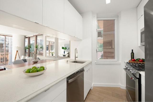 kitchen with stainless steel appliances, a sink, light wood-type flooring, light countertops, and white cabinetry