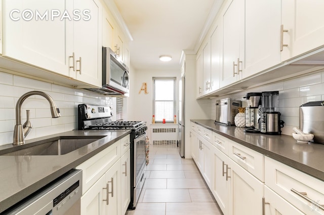 kitchen with a sink, appliances with stainless steel finishes, radiator heating unit, and tasteful backsplash