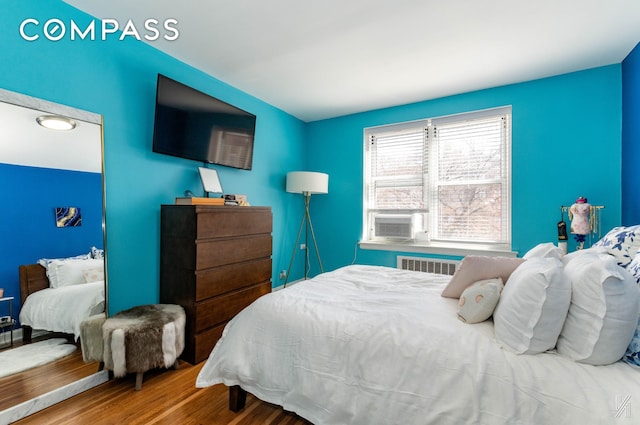 bedroom with radiator, wood finished floors, and cooling unit