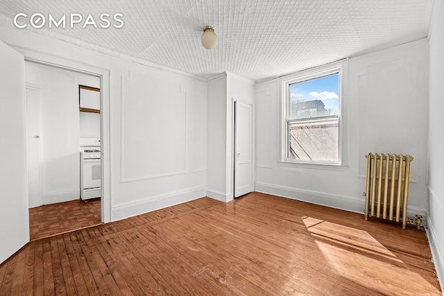 unfurnished bedroom with radiator, wood finished floors, and baseboards