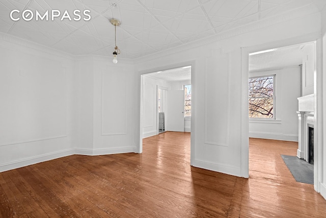 interior space with baseboards, crown molding, a fireplace with flush hearth, an ornate ceiling, and light wood-style flooring