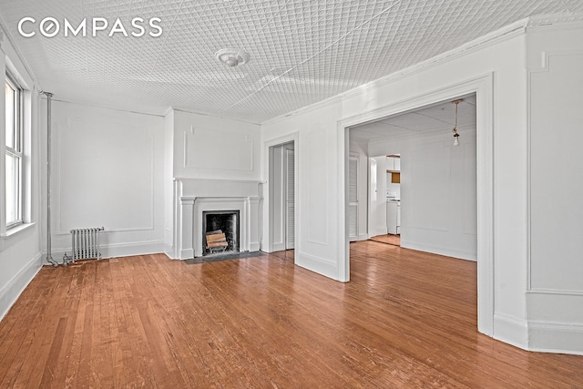 unfurnished living room with a fireplace with flush hearth, wood finished floors, and a decorative wall