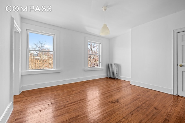 unfurnished room featuring radiator heating unit, wood-type flooring, and baseboards