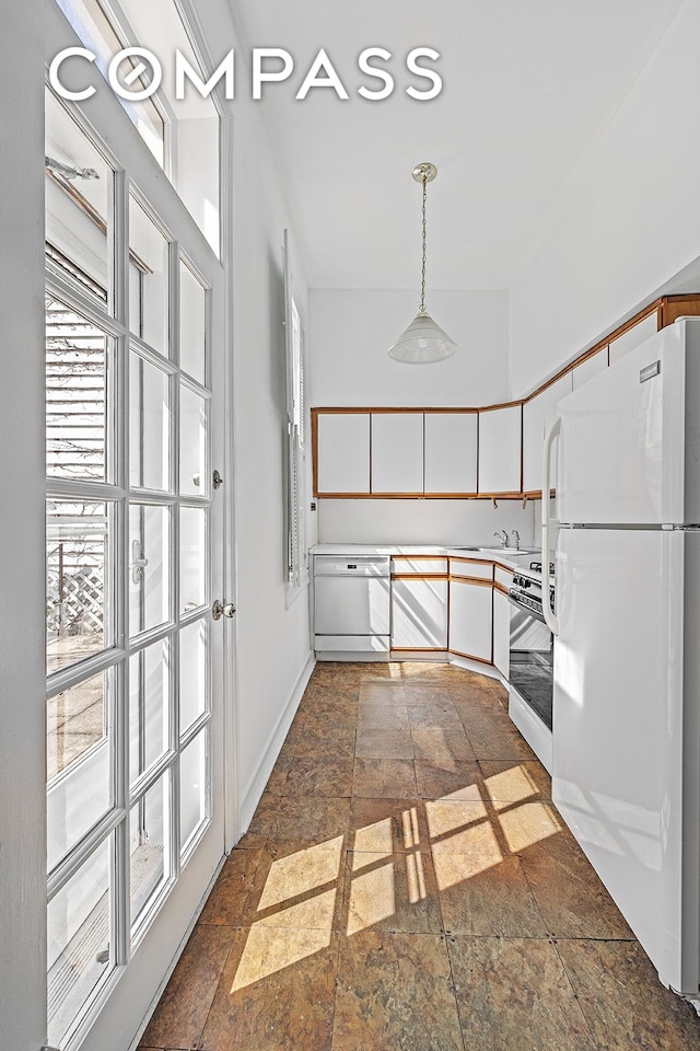 kitchen featuring white appliances, stone tile floors, white cabinets, hanging light fixtures, and baseboards